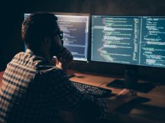 Microsoft affords SDK for testing framework A developer works across multiple displays showing lines of code in a dimly lit workspace.