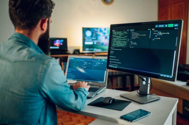 Back view of a senior developer typing code and programming a new generation of AI bots and AI generators at the home office. Artificial intelligence development and programming AI bots.