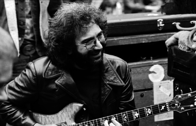 A black-and-white photo of Jerry Garcia playing guitar.