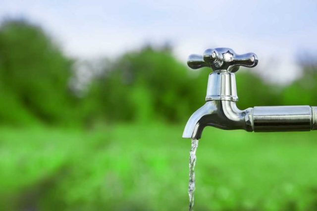 shutterstock 434035804 water flowing from a silver outdoor tap amid green fields and green trees