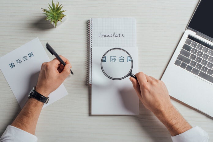 cropped view of translator working with hieroglyphics, laptop and magnifying glass