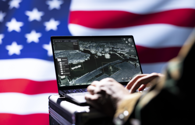 Soldier using a laptop running a military software on a background of the US flag.