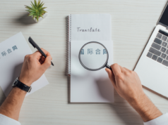 Literary World Divided As Simon & Schuster’s Dutch Arm Spend… View of a translator holding a magnifying glass on a note while writing on the other hand.