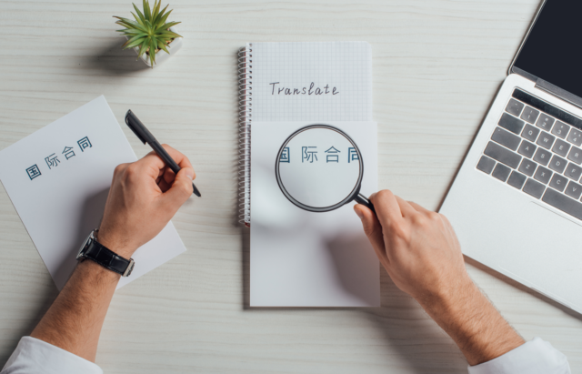 View of a translator holding a magnifying glass on a note while writing on the other hand.