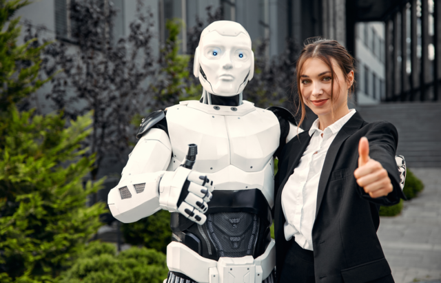 A humanoid robot and a woman making a thumbs up sign.