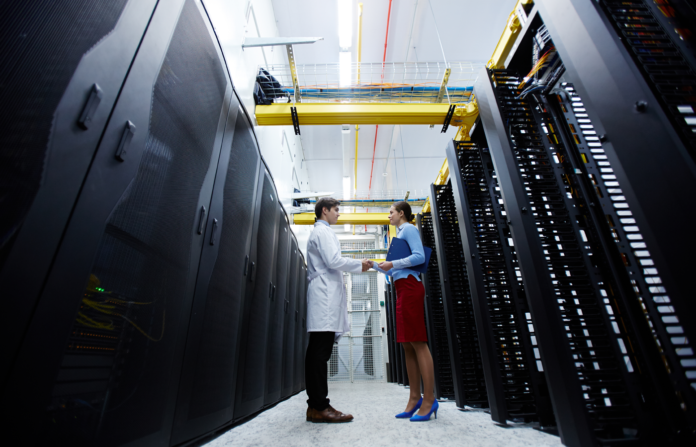 IT professionals shaking hands on a server room hallway.