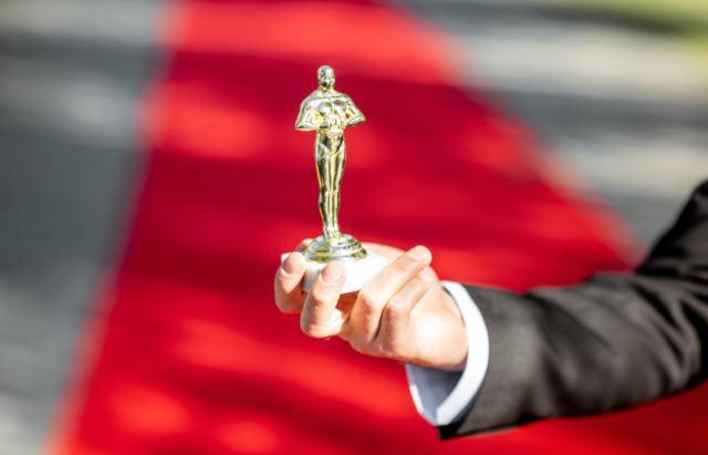 1737559986_Oscar-Nominated-Film-Editor’s-AI-Use-Might-Cost-It-the-Acade.png Person holding an award statue on a red carpet walk background.