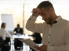 Why enterprises fail at finops man reading a document and rubbing his forehead indicating stress worry concern with people meeting around a table in the background