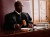 Experienced male judge with wooden gavel over sounding block sitting by desk.