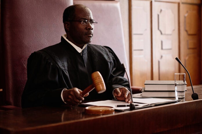 Experienced male judge with wooden gavel over sounding block sitting by desk.
