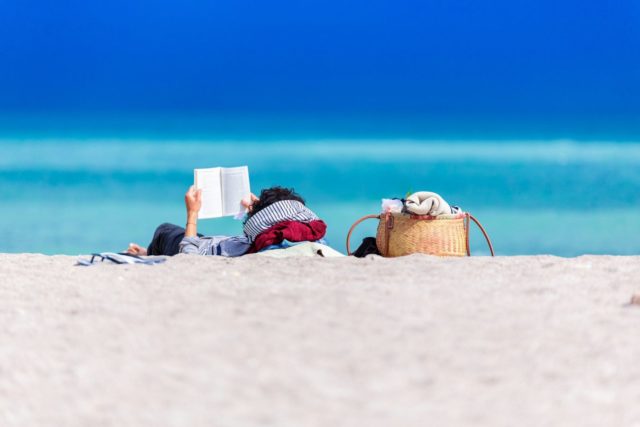 1747874331_Summer-Reading-Picks-That-Dont-Exist-Chicago-Sun-Times-Apo.jpg A person lying on shore reading a book.