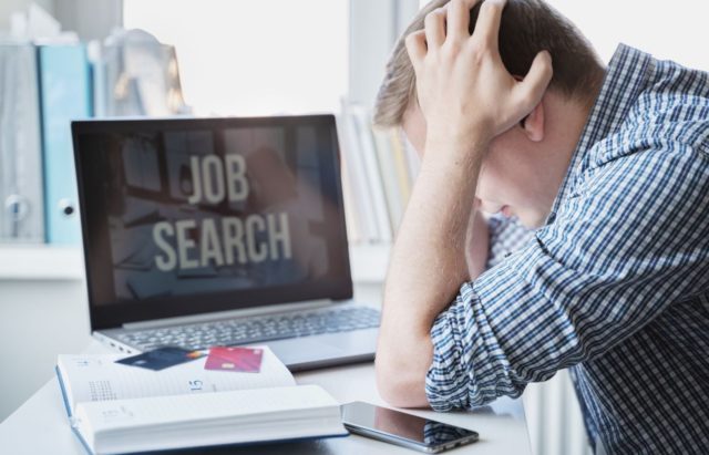 1748523405_Anthropic-CEO-AI-Will-Soon-Take-Nearly-Half-of-Entry-Level.jpg Man holds head with hands on table with laptop. Looking for remote work.