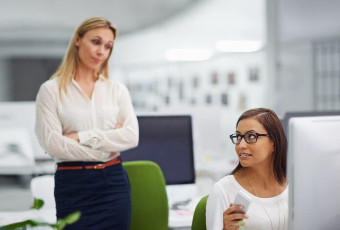 Stock photo of two workers in an office with one person appearing to look at the other with judgment.