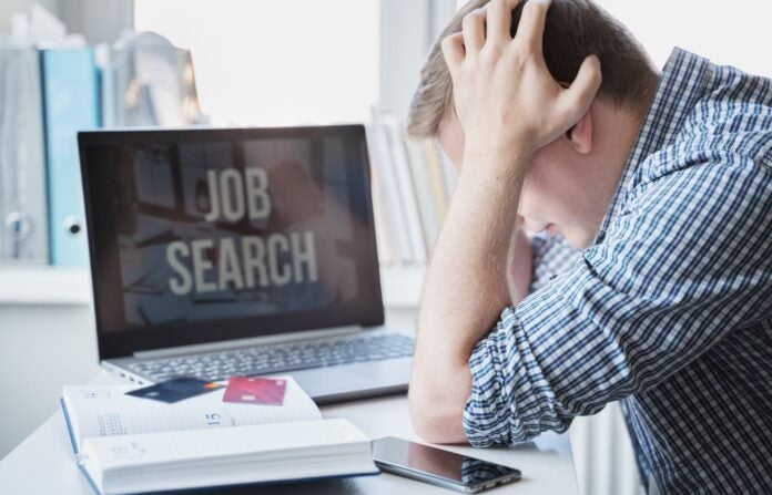 Man holds head with hands on table with laptop. Looking for remote work.
