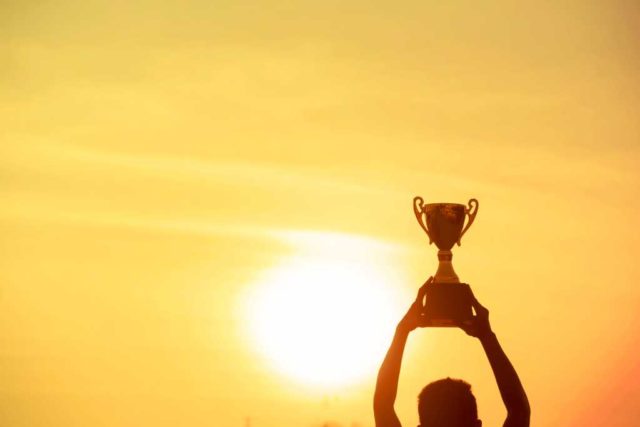 How-GitHub-won-software-development.jpg Winner holding golden trophy cup above head sun and golden sky in background