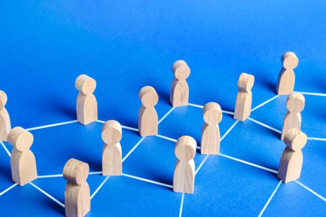 How-multi-agent-collaboration-is-redefining-real-world.jpg Wooden figures of people connected by lines in a social network. White lines on blue background.