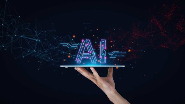 Before-you-build-your-first-enterprise-AI-app.jpg A human hand against a midnight-black background holds a tablet like a platter with the word "AI" resting on top. AI tools, AI technology, AI innovation.