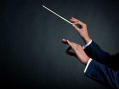 How Ansible does the true work in hyperautomation The hands of a male orchestra conductor directing with his baton in concert. Ivory baton white cuffs and dark blue suit against a dark gray background.