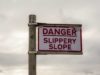 AI brokers and unhealthy productiveness metrics Sign post reading, Danger Slippery Slope. Warning sign near seafront on overcast day.