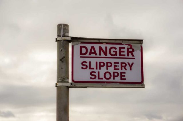 Sign post reading, Danger Slippery Slope. Warning sign near seafront on overcast day.