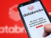 Databricks launches Genie Code to automate information science… A photograph of a Databricks website on a phone being held in front of a larger, blurry version of the Databricks logo.