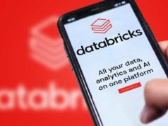 Databricks launches Genie Code to automate information science… A photograph of a Databricks website on a phone being held in front of a larger, blurry version of the Databricks logo.