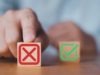 Save cash by canceling extra software program tasks, says… Two building blocks pictured, one with a green check mark and the other with a red x, standing for cancelation. The x is pushed to the foreground by a human hand.