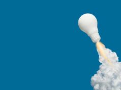 An explosion of software program is coming white light bulb blasts off like a rocket trailing fire and smoke against a blue background