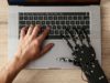 SpaceXAI launches Grok 4.5, touts decrease coding-task… image of a human and robot hand typing at a laptop