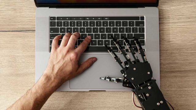 SpaceXAI-launches-Grok-4.5-touts-lower-coding-task.jpg image of a human and robot hand typing at a laptop
